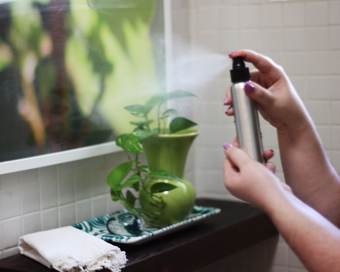 Person holding a spray bottle in front of a shelf with wall art in the background